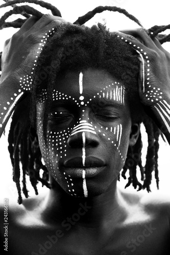 Portrait of young african man with dreadlocks and traditional face paint, hands pulling his hair, black and white