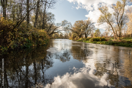 tiver tributary with sky mirroring, colorful trees and blue sky with clouds during nice autumn day