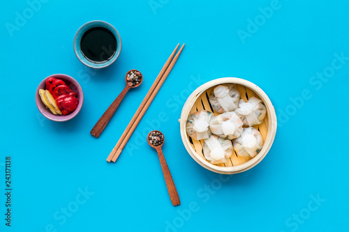 Dim sums with red pepper and vegetables with sticks and black tea in Chinese restaurant on blue background top view