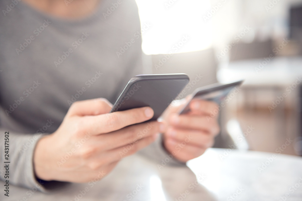 Young woman shopping online with credit card using smartphone at home. Indoor.