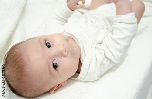 Cute tree months old baby boy dressed in white body looking at the camera while laying on the baby changer