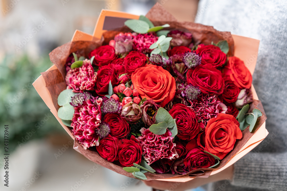 Fototapeta premium piękny świeży bukiet ciętych mieszanych kwiatów w ręce kobiety. praca kwiaciarni w kwiaciarni. Jasne soczyste czerwone kolory