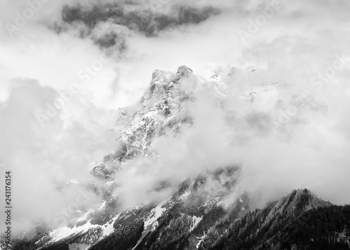 Monochrome image, snowcapped mountain peak shrouded in clouds in Austria.