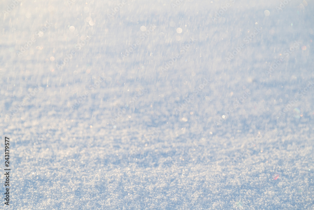 Close-up of fresh snow on the ground and blurred snowfall with bokeh on a sunny day. Good as a winter season background. Shallow depth of field, blurred background.