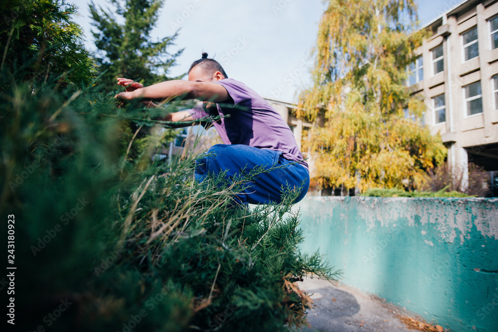 Young parkour guy jumping over a concrete wall and landing on another concrete wall while doing tricks in the air. Young parkour guy jumping over a concrete wall and landing on another concrete wall while doing tricks in the air.