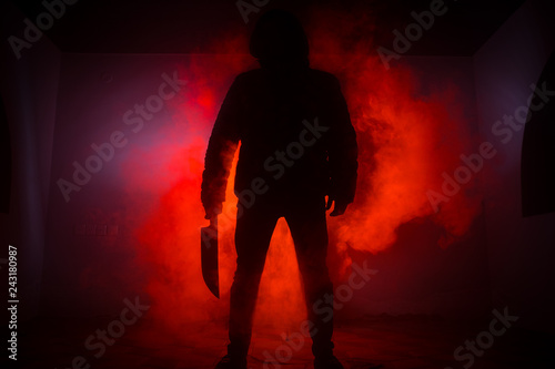 A dangerous hooded man standing in the dark and holding a knife. Face can not be seen. Committing a crime concept. Selective focus photo