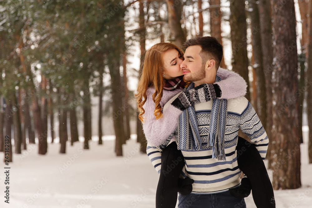Winter, couple in love. Young man and woman embracing in snowy forest. Romantic couple in winter wear enjoying snowfall. Love story in the winter forest