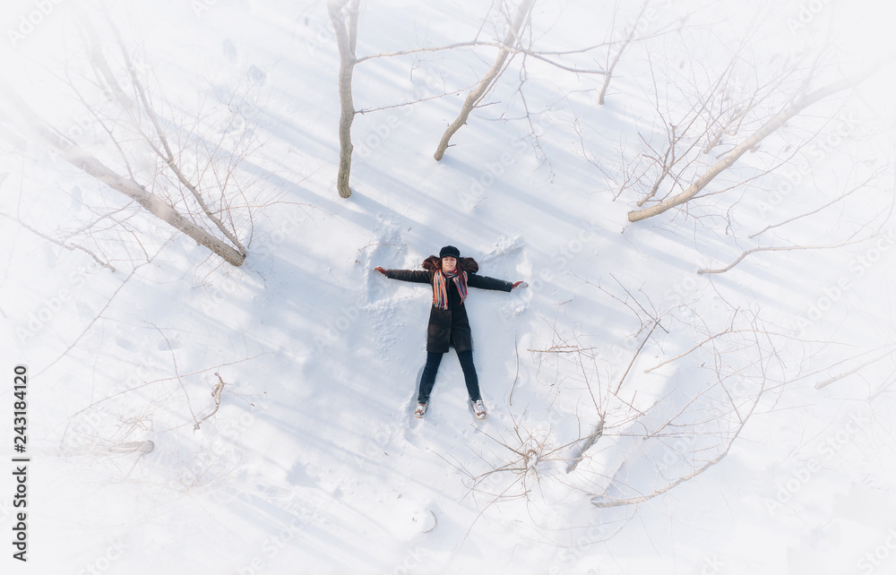 A girl on the snow shows an angel. Spreading arms. Top view. Drone.