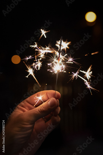 Burning sparkler in hand with blurred lights in the background