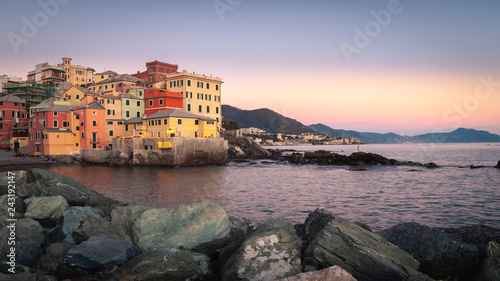 Genoa, Italy. Amazing panorama at sunset on the ancient fishing village of Boccadasse overlooking the sea. Rocks in the foreground. Background with Ligurian mountains and the promontory of Portofino