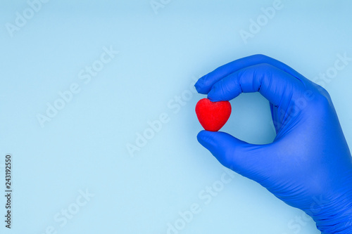 Health insurance or love concept. Hand of a cardiologist in a blue glove holds a red heart. Concept of cardiology and cardiovascular diseases.