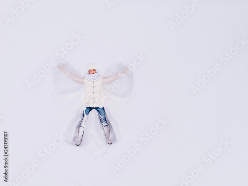 Top view aerial drone. Snow angel. Young girl lying snowdrift, waving his hands different directions photo