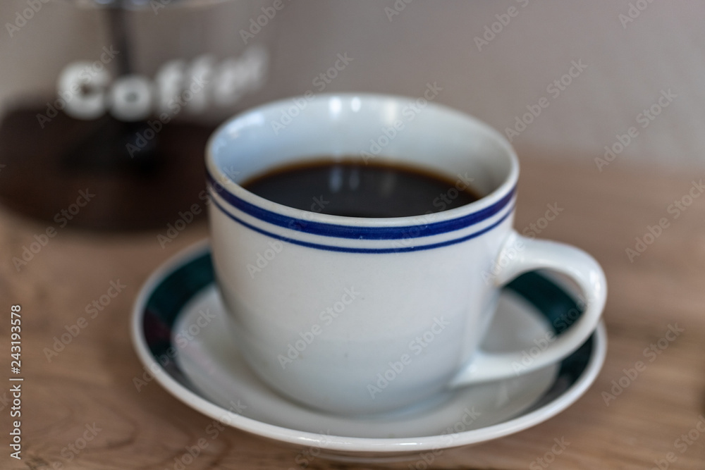 A cup of coffee with a blurred coffee jar