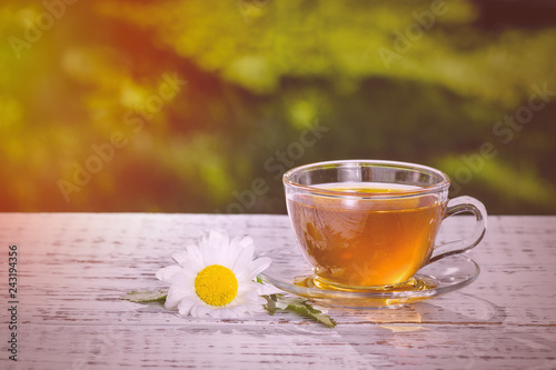 Environmentally friendly product. Cup of tea with chamomile, close-up, lit by sunlight, on a white wooden table. Chamomile tea.