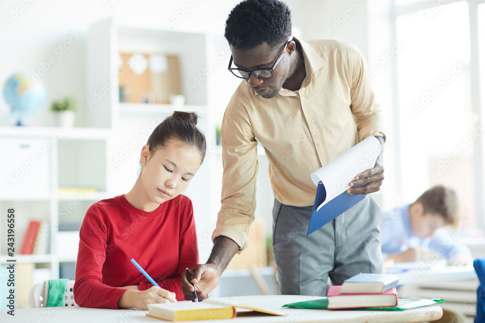 African-american teacher pointing at notes of schoolgirl while explaining her how to correct mistake African-american teacher pointing at notes of schoolgirl while explaining her how to correct mistake
