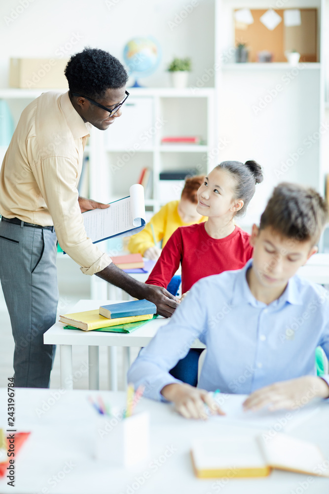 Young teacher explaining to one of pupils how to write word correctly during individual work Young teacher explaining to one of pupils how to write word correctly during individual work
