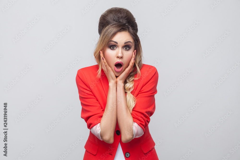 Portrait of surprised beautiful business lady with hairstyle and makeup in red fancy blazer, touching her face and looking at camera with amazed face. indoor studio shot, isolated on grey background. Portrait of surprised beautiful business lady with hairstyle and makeup in red fancy blazer, touching her face and looking at camera with amazed face. indoor studio shot, isolated on grey background.