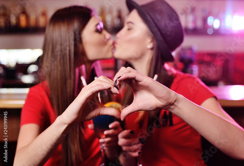 two cute young girlfriends kissing in a nightclub against the heart of the hands