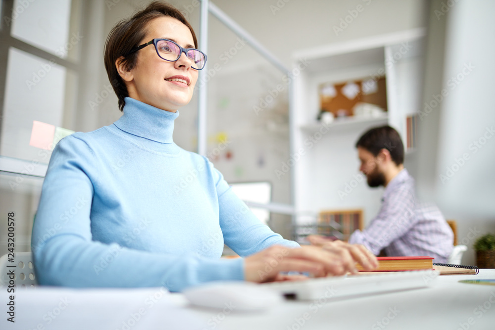Young designer or manager typing in front of computer screen while sitting by desk in working environment Young designer or manager typing in front of computer screen while sitting by desk in working environment