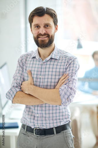 Young successful contemporary manager in shirt standing in front of camer swith crossed arms in office photo