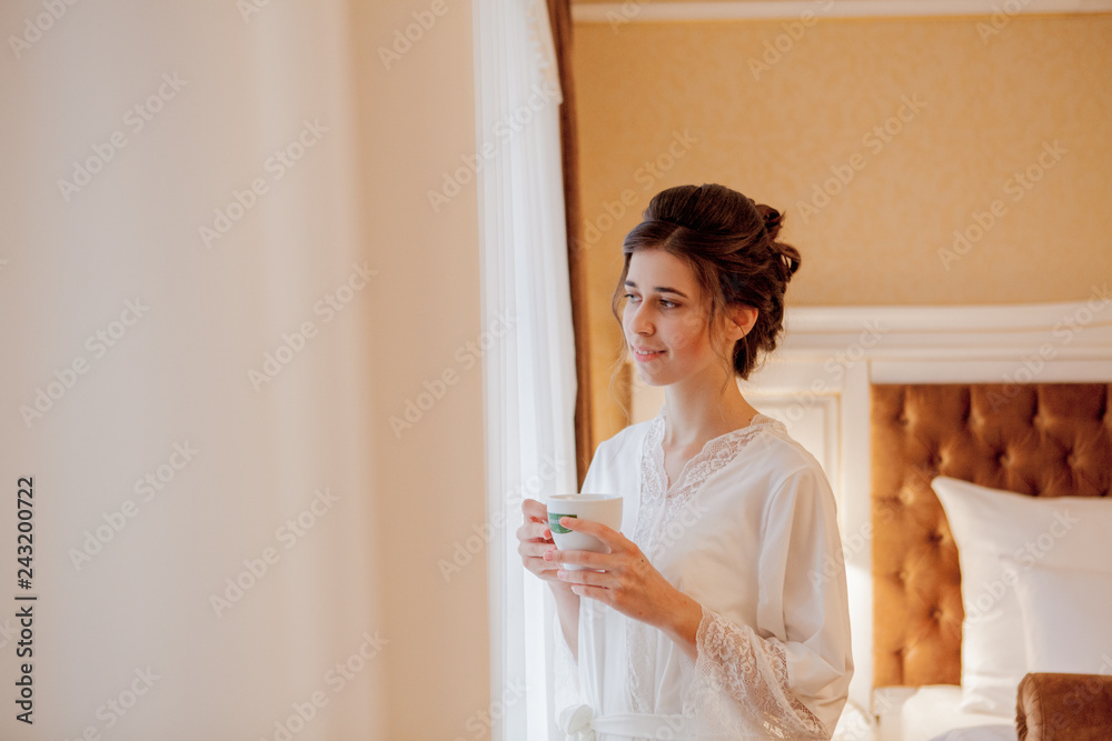 the bride is drinking coffee, bride holds a cup of coffee, bride in a white coat, morning of the bride, wedding day the bride is drinking coffee, bride holds a cup of coffee, bride in a white coat, morning of the bride, wedding day