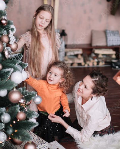 mom and her little daughters decorating the Christmas tree © yurolaitsalbert