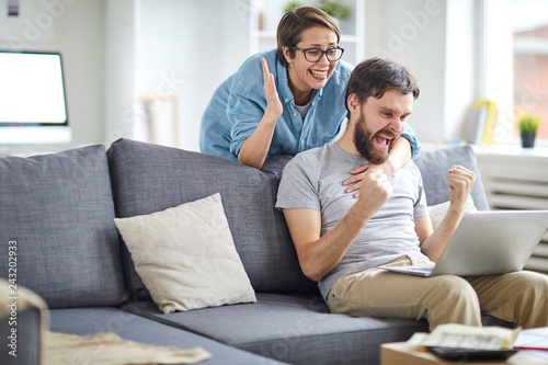 Glad and ecstatic couple expressing triumph while looking at names of winners in lottery on laptop display