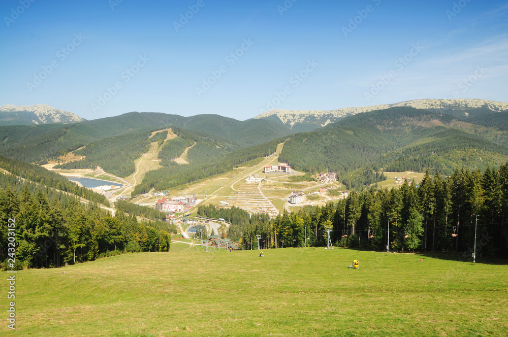 Mountains with forest, ski resort buildings, chairlifts and sky in the summer