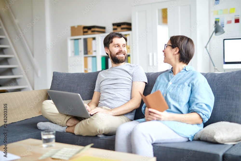 Cheerful young couple discussing where to go for vacations before reserving tickets online Cheerful young couple discussing where to go for vacations before reserving tickets online
