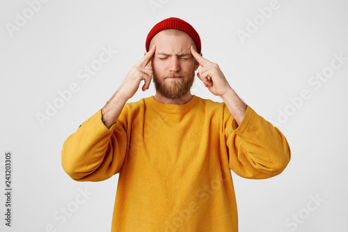 The guy holds fingers on temples, his eyes are squinting, trying to remember something. Bearded man feels headache, massages his temples with fingers, isolated on a white background. photo