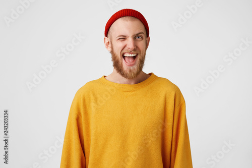 Photography Young man winks at the camera,mouth open, dressed in a yellow sweater and red hat