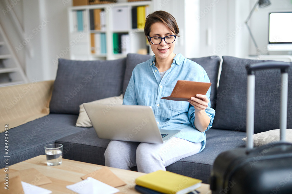 Young contemporary woman with laptop and passport ordering tickets online while looking forwards for vacation Young contemporary woman with laptop and passport ordering tickets online while looking forwards for vacation