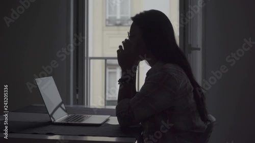 Silhouette of tired young woman with headache working with laptop. Side view of tired businesswoman working on project at home. Overwork concept