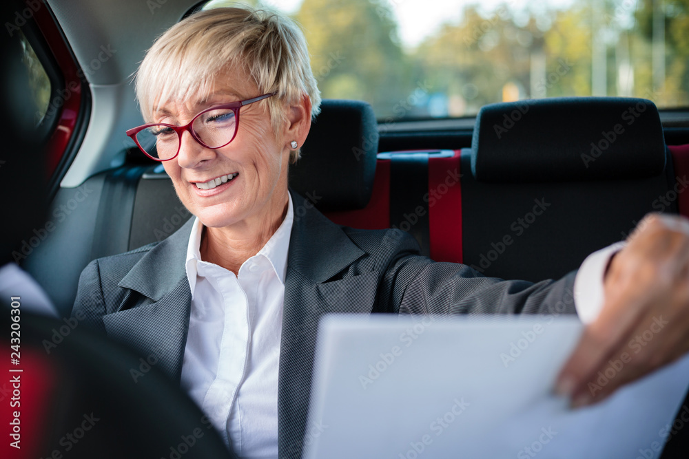 Successful senior manager looking at documents while traveling to an important meeting on a back seat of the car