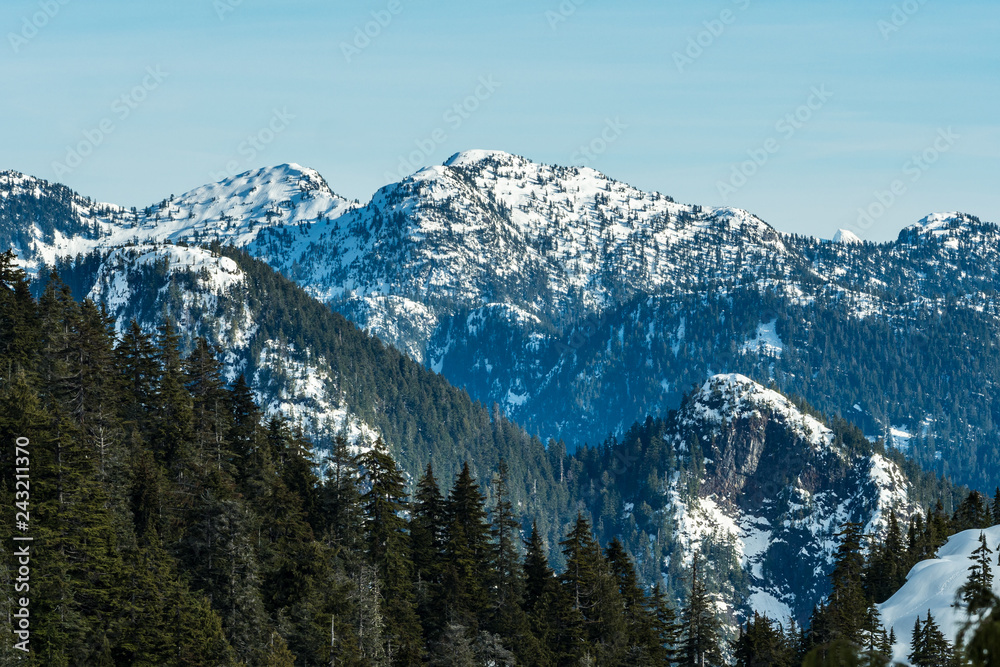 green forest covered mountain range under thin layer of snow behind forest on hill top under blue cloudy sky 