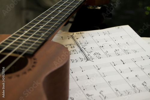 ukulele near a music sheet over a black and  reflecting piano surface