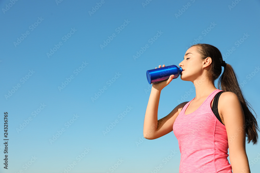 Young sporty woman drinking from water bottle outdoors on sunny day. Space for text Young sporty woman drinking from water bottle outdoors on sunny day. Space for text