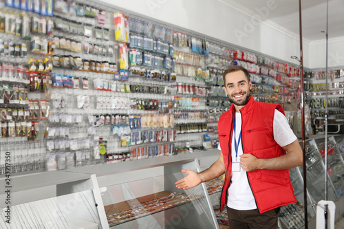 Salesman standing near showcase with fishing equipment in sports shop. Space for text