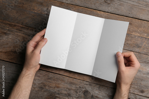 Man with blank brochure on wooden background, above view. Mock up for design