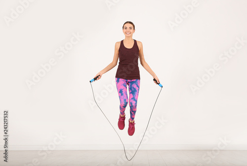 Full length portrait of young sportive woman training with jump rope in light room photo