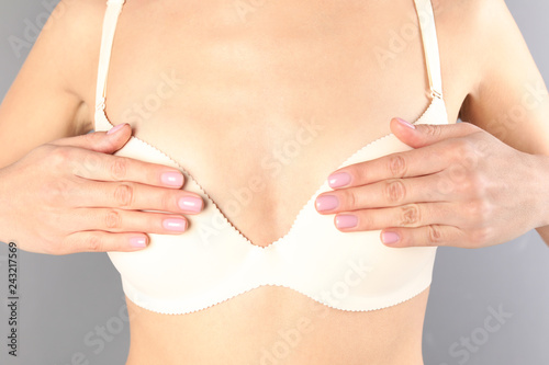 Young woman in white bra on gray background, closeup. Breast cosmetic surgery