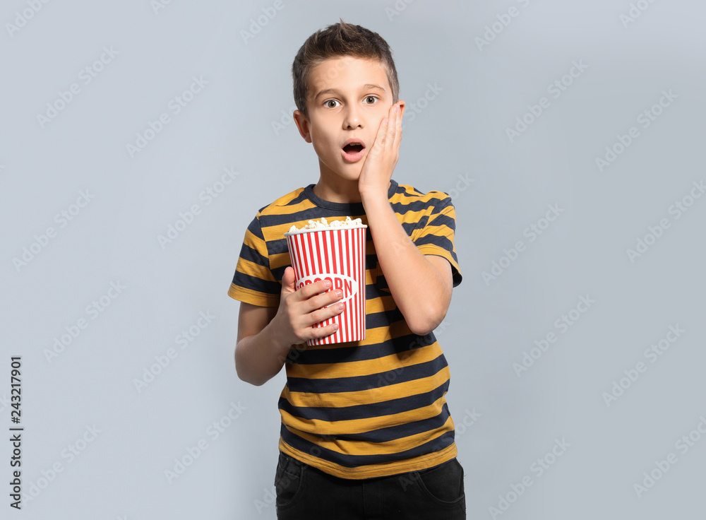 Naklejka premium Emotional boy with popcorn during cinema show on grey background