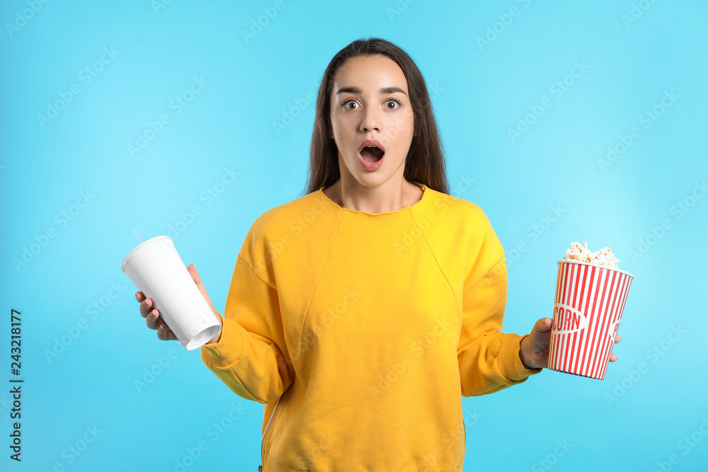 Fototapeta premium Emotional woman with popcorn and beverage during cinema show on color background