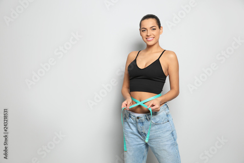 Slim woman in oversized jeans with measuring tape on light background, space for text. Weight loss