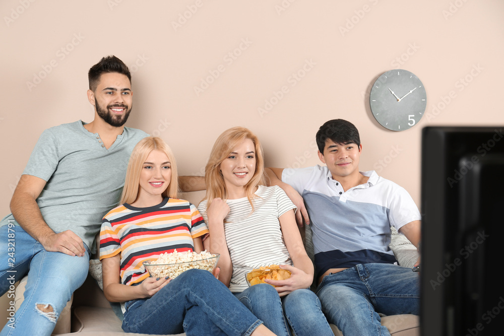 Young friends with snacks watching TV on sofa at home Young friends with snacks watching TV on sofa at home