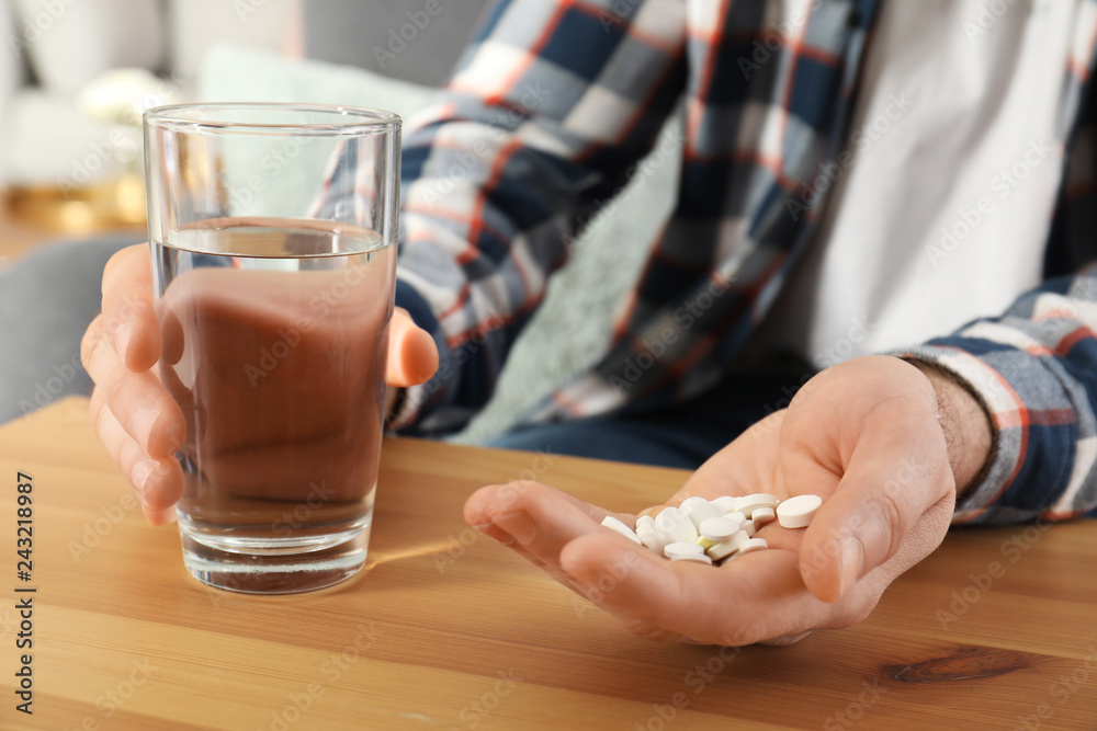 Man holding pills and glass of water at table, closeup Man holding pills and glass of water at table, closeup