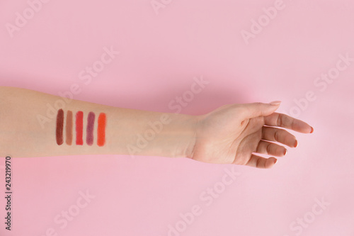 Woman with lipstick swatches on color background, closeup of hand