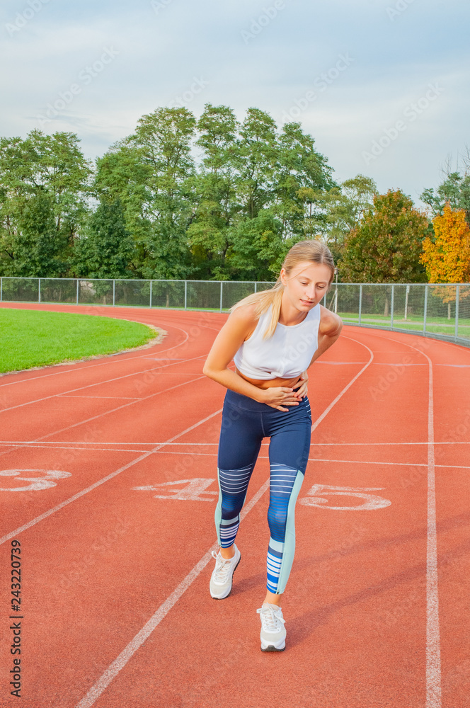 Woman on running track has side cramps during workout