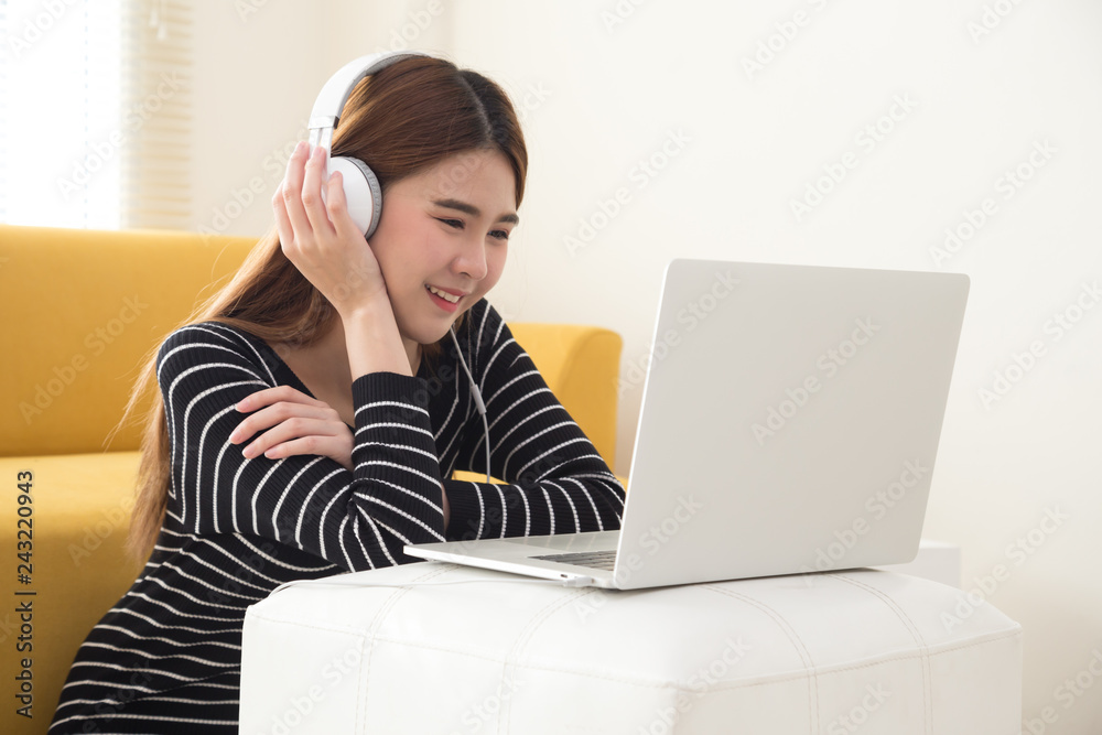 Young Asian student using laptop computer and sitting on floor in living room while listening and watching online coursework with electronic earphones or headphone. Internet E-Learning concept Young Asian student using laptop computer and sitting on floor in living room while listening and watching online coursework with electronic earphones or headphone. Internet E-Learning concept