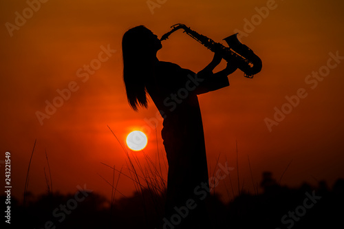 Silhouette of musician with saxophone sunset field,Saxophonist. woman playing on saxophone against the background of sunset 